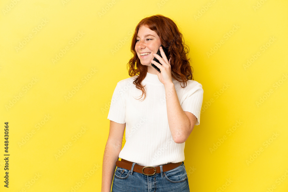 Teenager reddish woman isolated on yellow background keeping a conversation with the mobile phone Teenager reddish woman isolated on yellow background keeping a conversation with the mobile phone