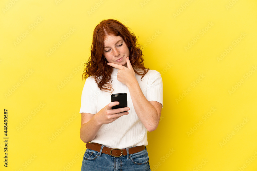 Teenager reddish woman isolated on yellow background thinking and sending a message Teenager reddish woman isolated on yellow background thinking and sending a message