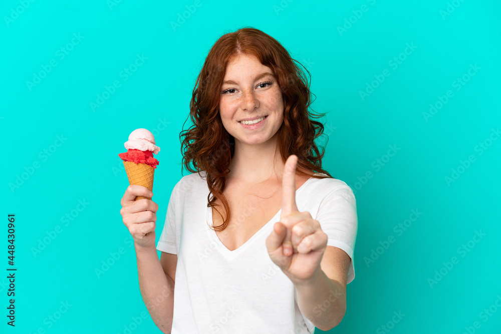 Teenager reddish woman with a cornet ice cream isolated on blue background showing and lifting a finger Teenager reddish woman with a cornet ice cream isolated on blue background showing and lifting a finger