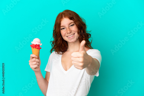 Teenager reddish woman with a cornet ice cream isolated on blue background with thumbs up because something good has happened