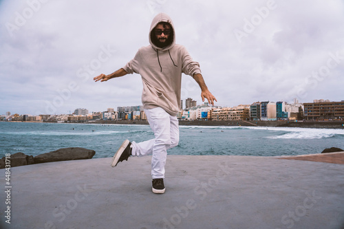 Young caucasian man, wearing casual clothes, dancing urban dances on the beach avenue
