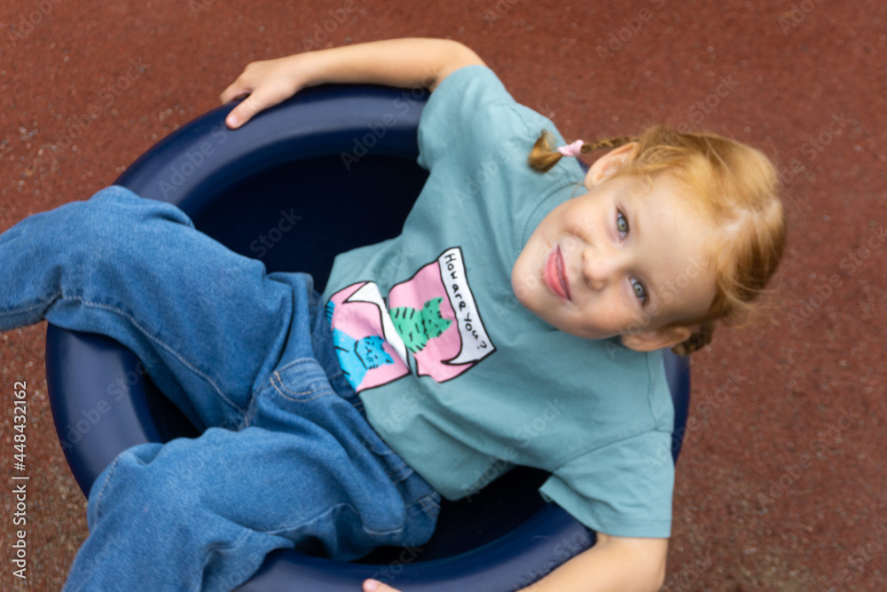 Naklejka premium Little Caucasian redhead girl swinging cheerfully on a swing.