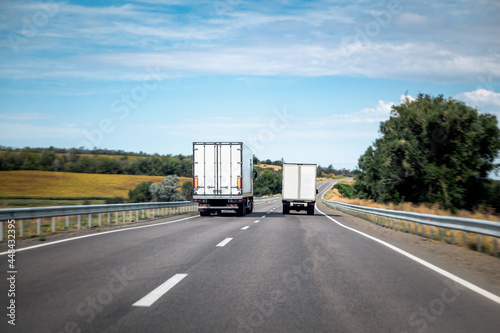 Two trucks drive forward into distance in daylight. Transport delivers cargo outside the city.