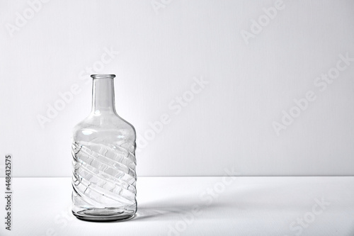 Glass empty open bottle with copy space. Graphic still life with light and shadow in white light. The concept of glass containers  recyclable materials or alcoholism. Large creative vase. Open flask