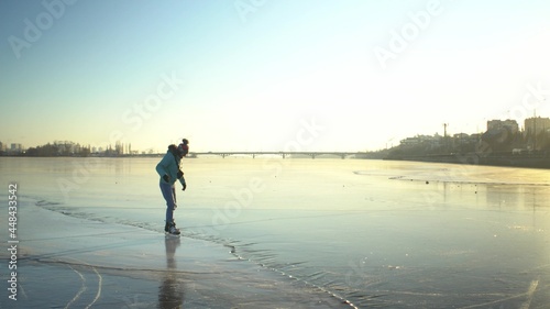 Adult caucasian woman in blue jacket skates on ice of frozen lake