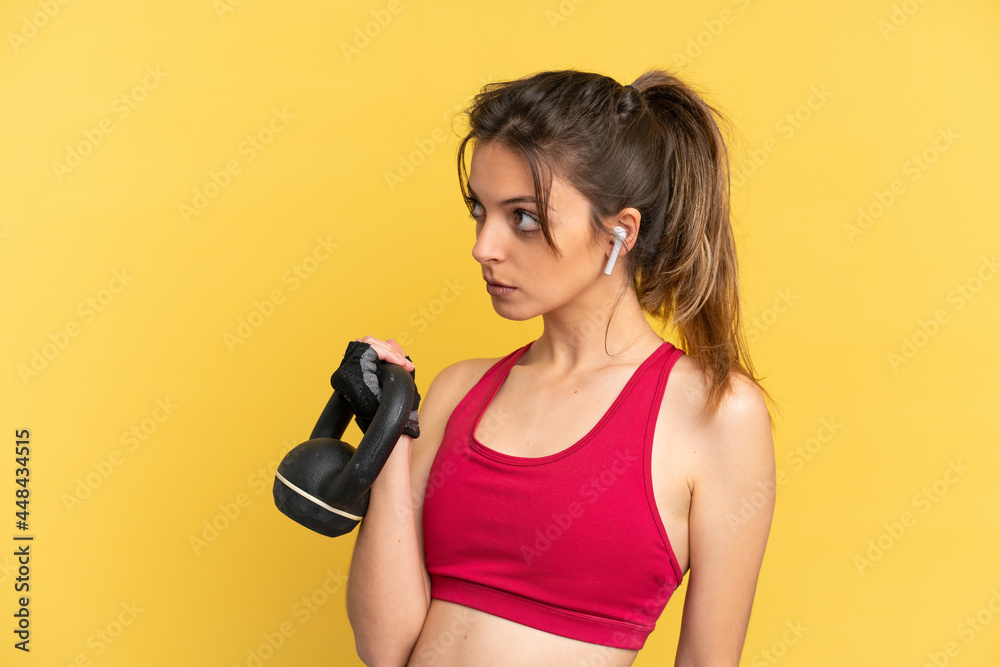 Young caucasian woman isolated on blue background making weightlifting with kettlebell Young caucasian woman isolated on blue background making weightlifting with kettlebell