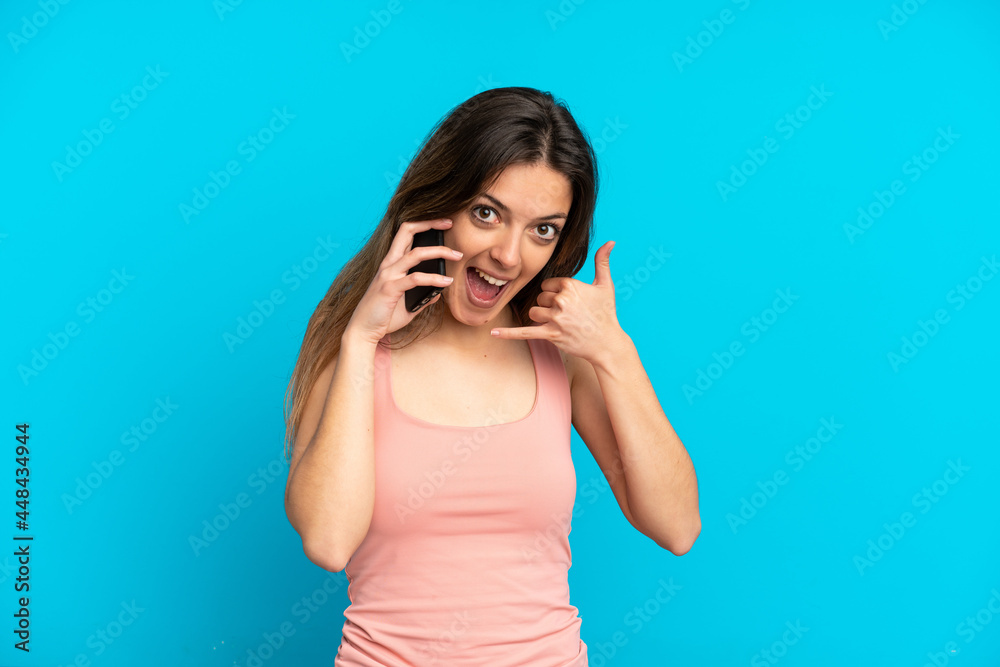 Young caucasian woman using mobile phone isolated on blue background making phone gesture. Call me back sign Young caucasian woman using mobile phone isolated on blue background making phone gesture. Call me back sign