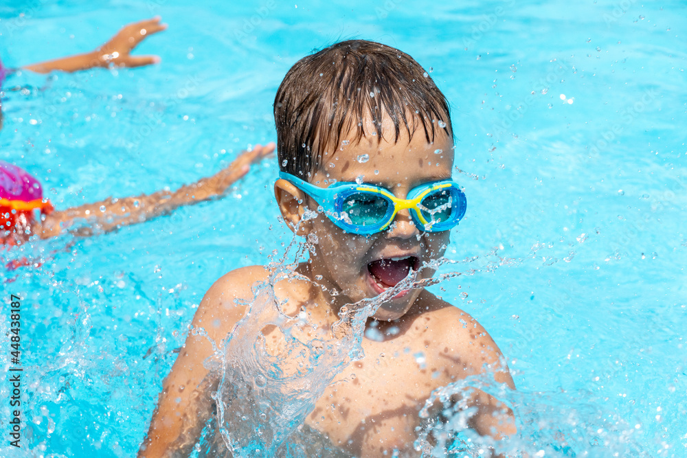 Naklejka premium Little child swims in the pool, plays splashing water