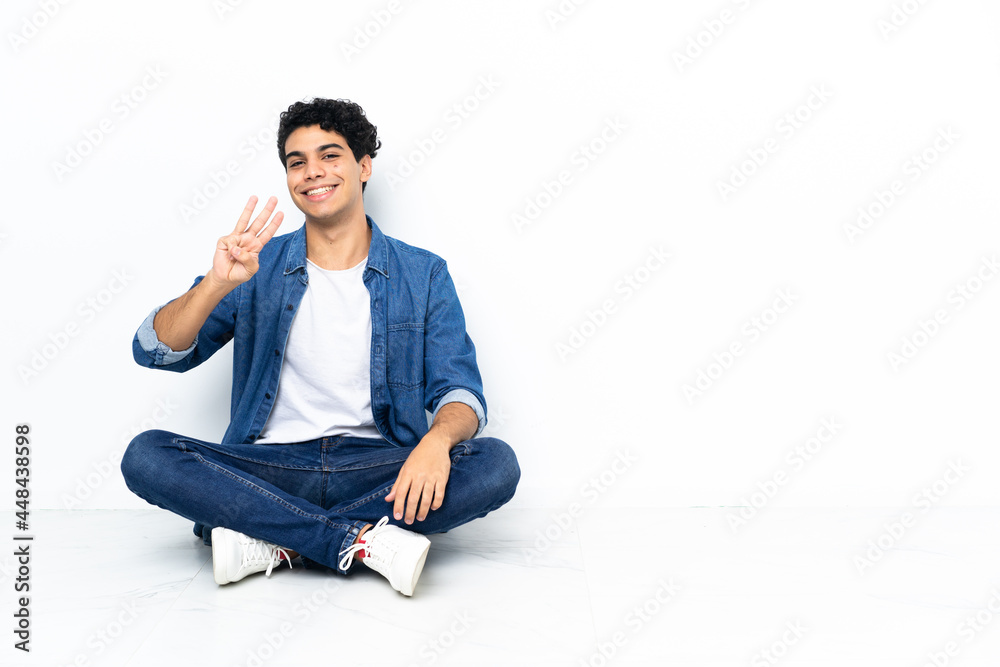 Venezuelan man sitting on the floor happy and counting three with fingers Venezuelan man sitting on the floor happy and counting three with fingers
