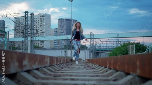 Young blonde woman walks on the railroad tracks in the city
