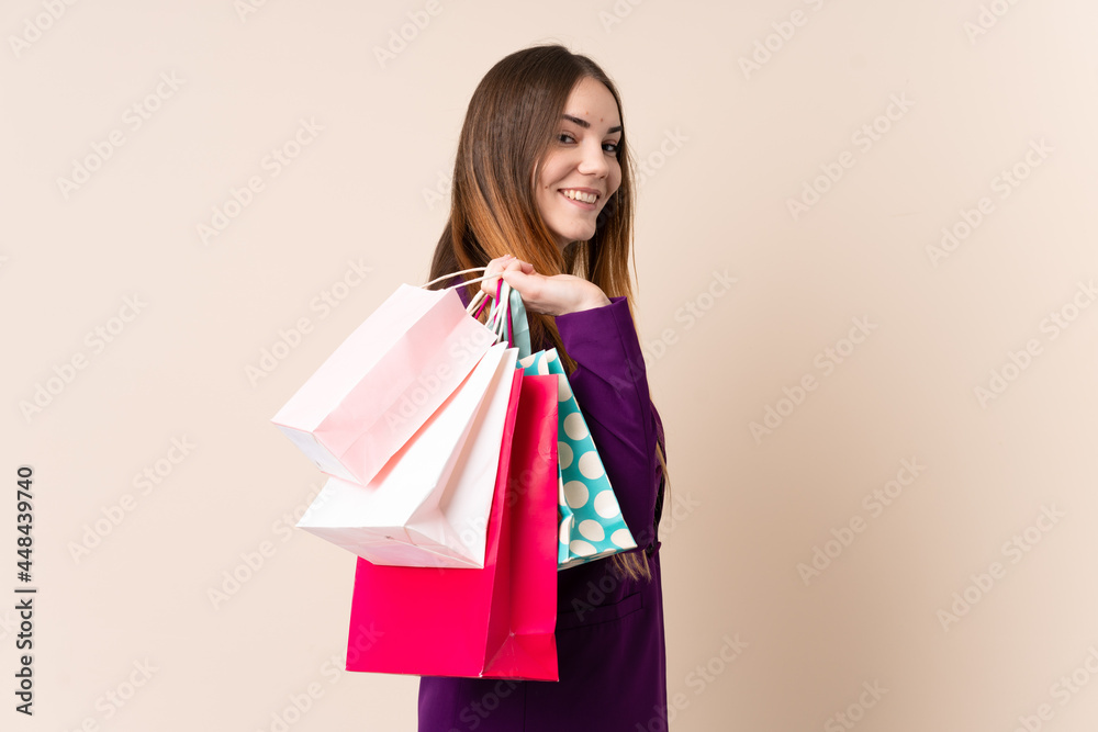 Young caucasian woman isolated on beige background holding shopping bags and smiling