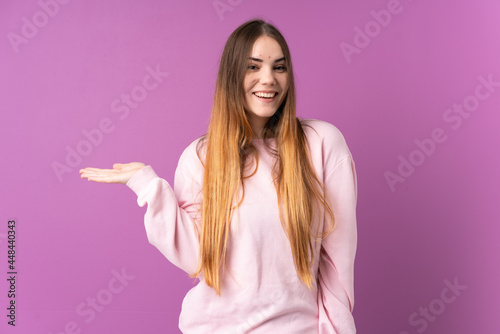 Young caucasian woman isolated on purple background holding copyspace imaginary on the palm to insert an ad