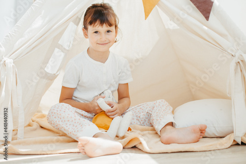 Six years cute girl playing in teepee with fabric tilda bunny at home photo