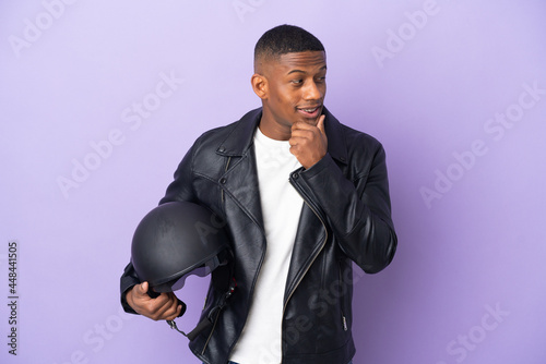 Latin man with a motorcycle helmet isolated on purple background looking to the side and smiling