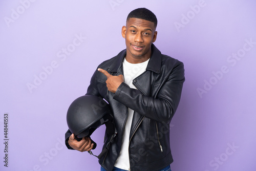 Latin man with a motorcycle helmet isolated on purple background pointing to the side to present a product