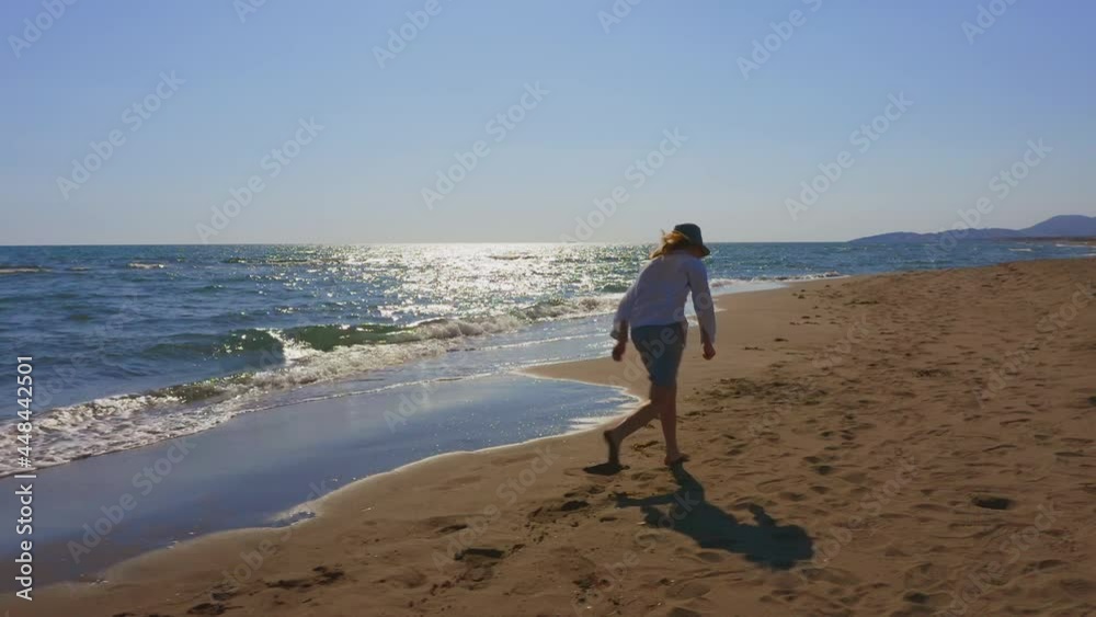 Tracking view of long hair boy barefoot running on sandy beach. Back view on kid in summer clothes enjoying vacation at sea. Tracking view of long hair boy barefoot running on sandy beach. Back view on kid in summer clothes enjoying vacation at sea.