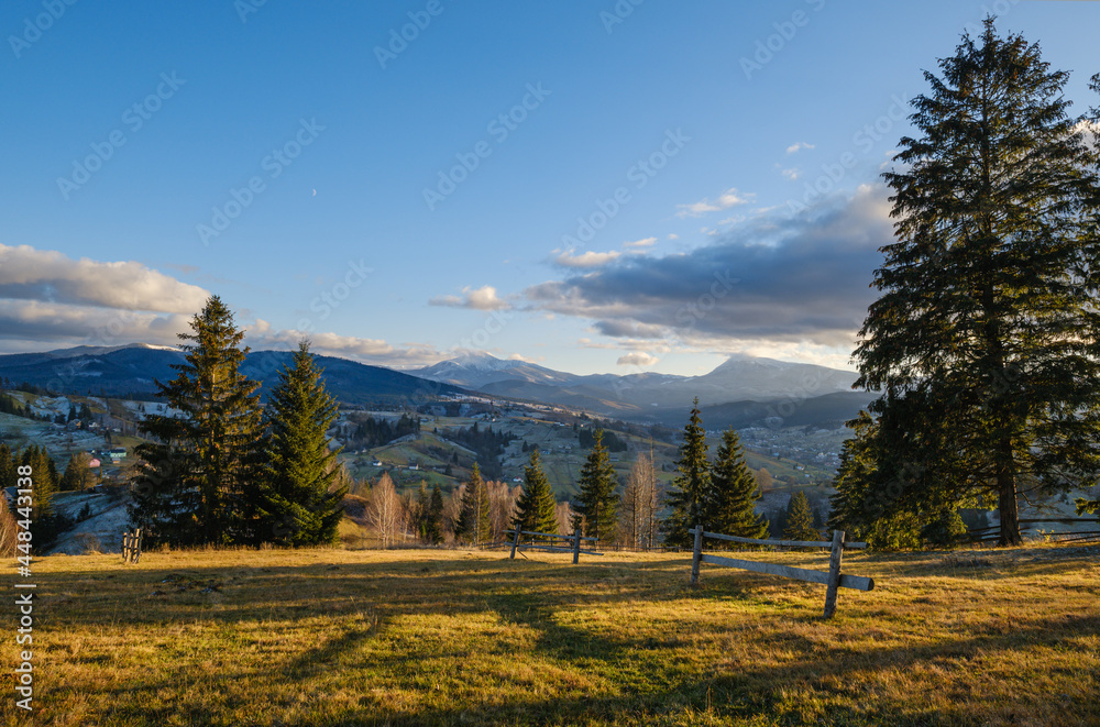 Late autumn mountain pre sunset scene with snow covered tops in far. Picturesque traveling, seasonal, nature and countryside beauty concept scene. Carpathians, Ukraine.