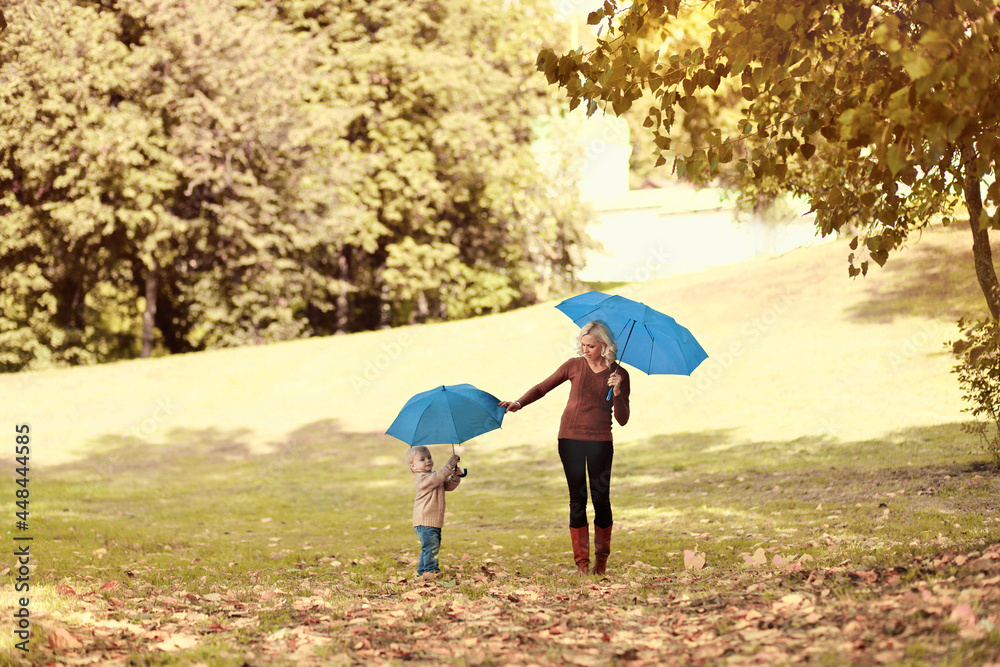 Mother and child walking together with umbrellas in autumn park on background of yellow leaves Mother and child walking together with umbrellas in autumn park on background of yellow leaves