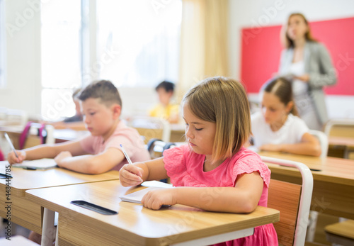 Portrait of cute intelligent schoolgirl who writing exercises at lesson in primary school