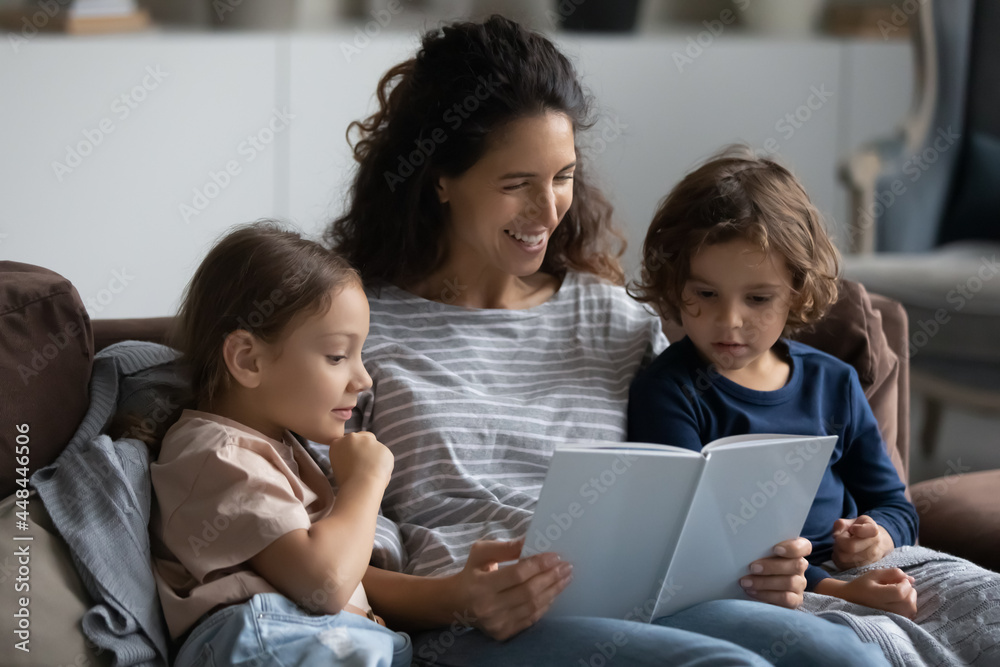 Happy mom reading book to little son and daughter, relaxing with kids together on couch. Mother enjoying leisure time with children, telling funny fairy tale for imagination development Happy mom reading book to little son and daughter, relaxing with kids together on couch. Mother enjoying leisure time with children, telling funny fairy tale for imagination development