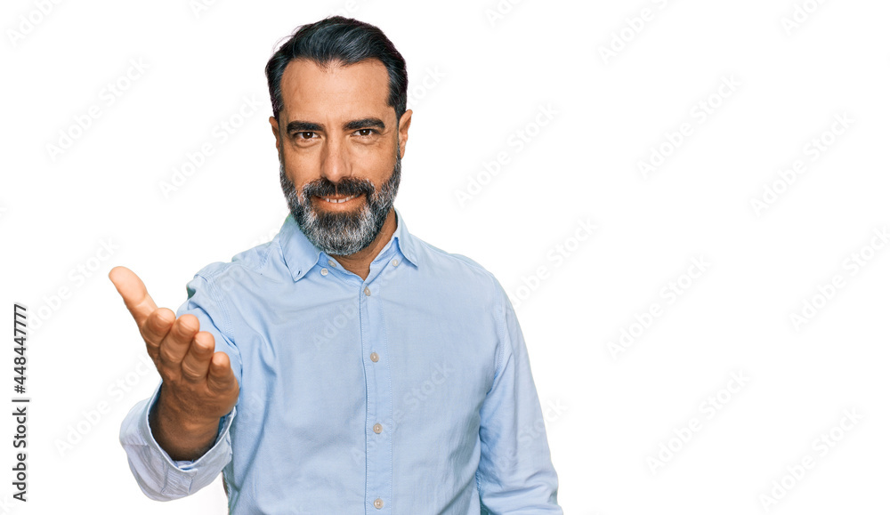 Middle aged man with beard wearing business shirt smiling friendly offering handshake as greeting and welcoming. successful business. Middle aged man with beard wearing business shirt smiling friendly offering handshake as greeting and welcoming. successful business.