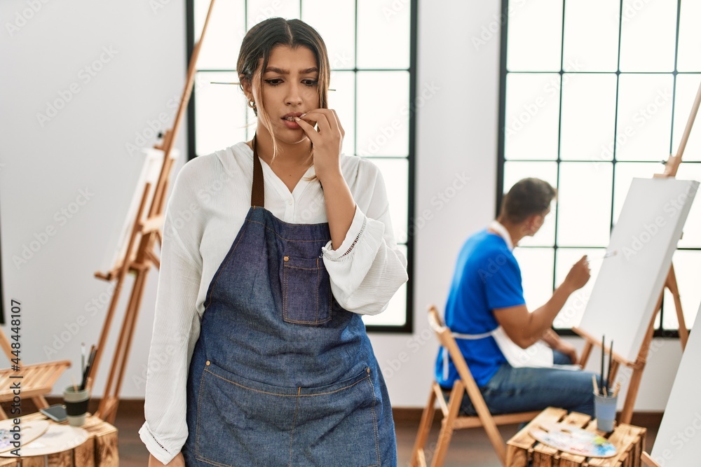 Young hispanic couple at art studio looking stressed and nervous with hands on mouth biting nails. anxiety problem. Young hispanic couple at art studio looking stressed and nervous with hands on mouth biting nails. anxiety problem.