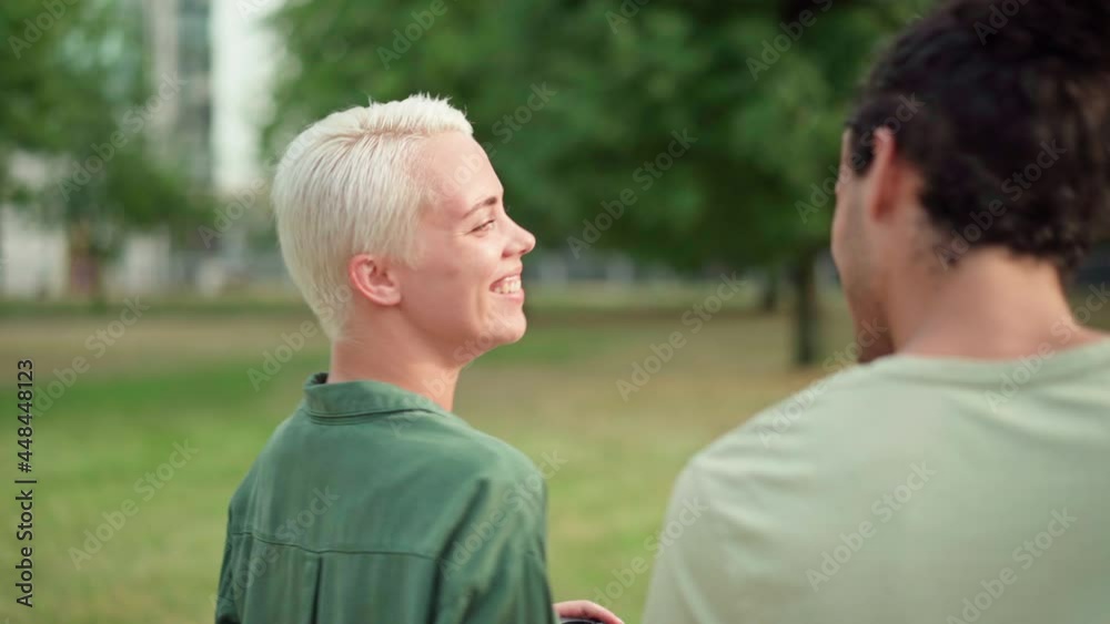 Side view tracking shot of cheerful woman with short hair enjoying walking and talking with her boyfriend in park. Smiling couple holding takeout coffee cups on date Side view tracking shot of cheerful woman with short hair enjoying walking and talking with her boyfriend in park. Smiling couple holding takeout coffee cups on date