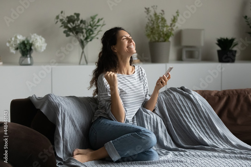 Konstfotografi Joyful exited Latin woman holding mobile phone, making winner yes hand gesture