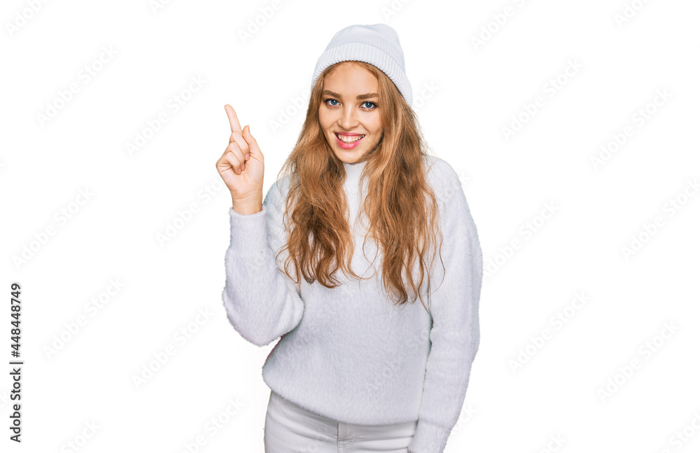 Young caucasian girl wearing wool sweater and winter cap showing and pointing up with finger number one while smiling confident and happy. Young caucasian girl wearing wool sweater and winter cap showing and pointing up with finger number one while smiling confident and happy.