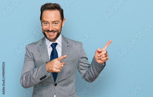 Middle age man wearing business clothes smiling and looking at the camera pointing with two hands and fingers to the side.