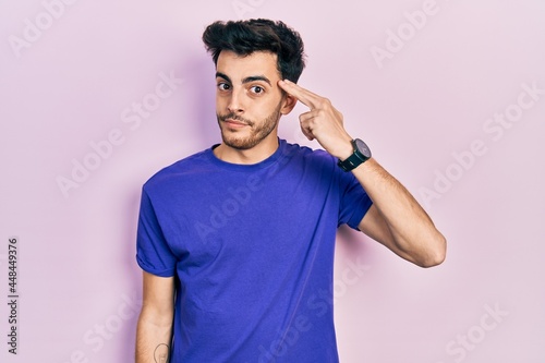 Young hispanic man wearing casual t shirt shooting and killing oneself pointing hand and fingers to head like gun, suicide gesture.