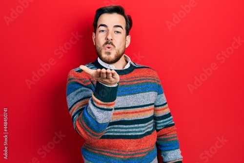 Handsome caucasian man with beard wearing elegant wool winter sweater looking at the camera blowing a kiss with hand on air being lovely and sexy. love expression.