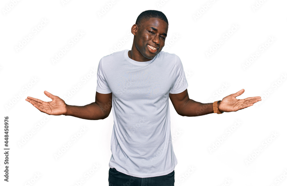 Young african american man wearing casual white t shirt smiling showing both hands open palms, presenting and advertising comparison and balance Young african american man wearing casual white t shirt smiling showing both hands open palms, presenting and advertising comparison and balance