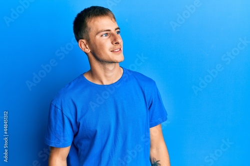 Young caucasian man wearing casual blue t shirt looking away to side with smile on face, natural expression. laughing confident.