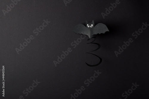 A bat on a black background has a place for text. A greeting card for Halloween. Craft made of paper.