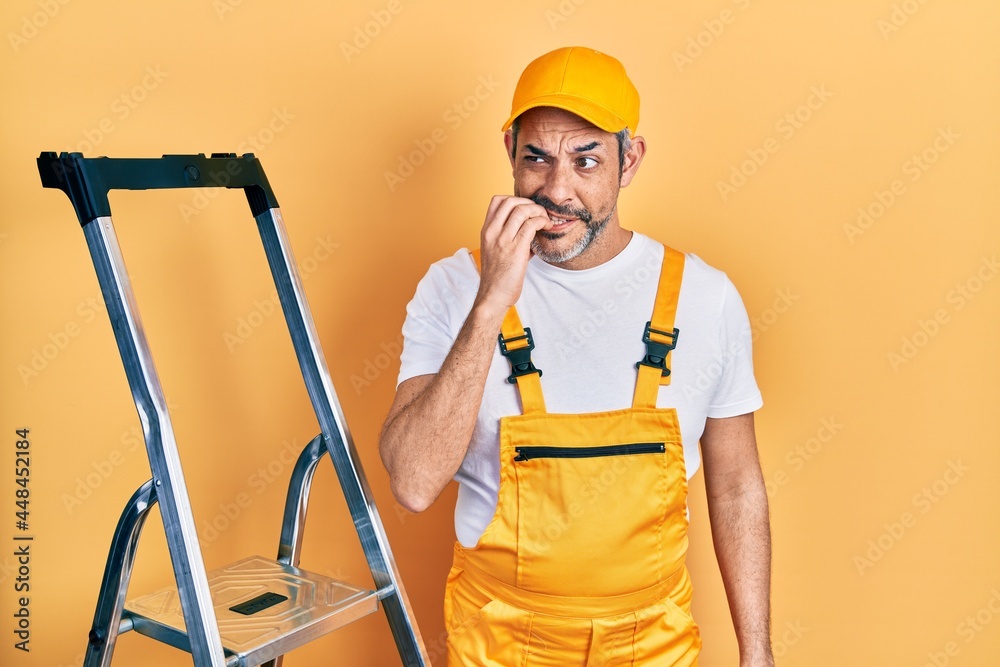 Handsome middle age man with grey hair holding ladder looking stressed and nervous with hands on mouth biting nails. anxiety problem. Handsome middle age man with grey hair holding ladder looking stressed and nervous with hands on mouth biting nails. anxiety problem.