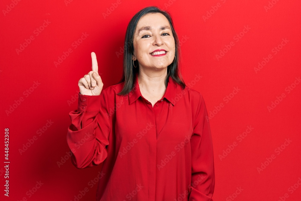 Middle age hispanic woman wearing casual clothes showing and pointing up with finger number one while smiling confident and happy. Middle age hispanic woman wearing casual clothes showing and pointing up with finger number one while smiling confident and happy.