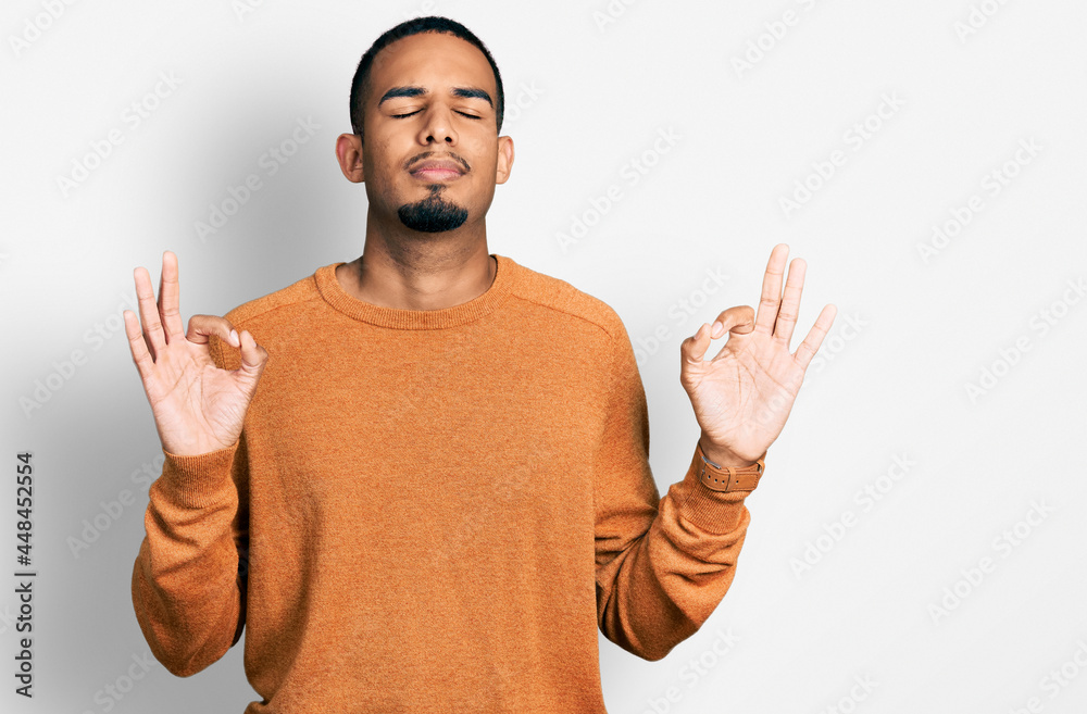 Young african american man wearing casual clothes relaxed and smiling with eyes closed doing meditation gesture with fingers. yoga concept. Young african american man wearing casual clothes relaxed and smiling with eyes closed doing meditation gesture with fingers. yoga concept.