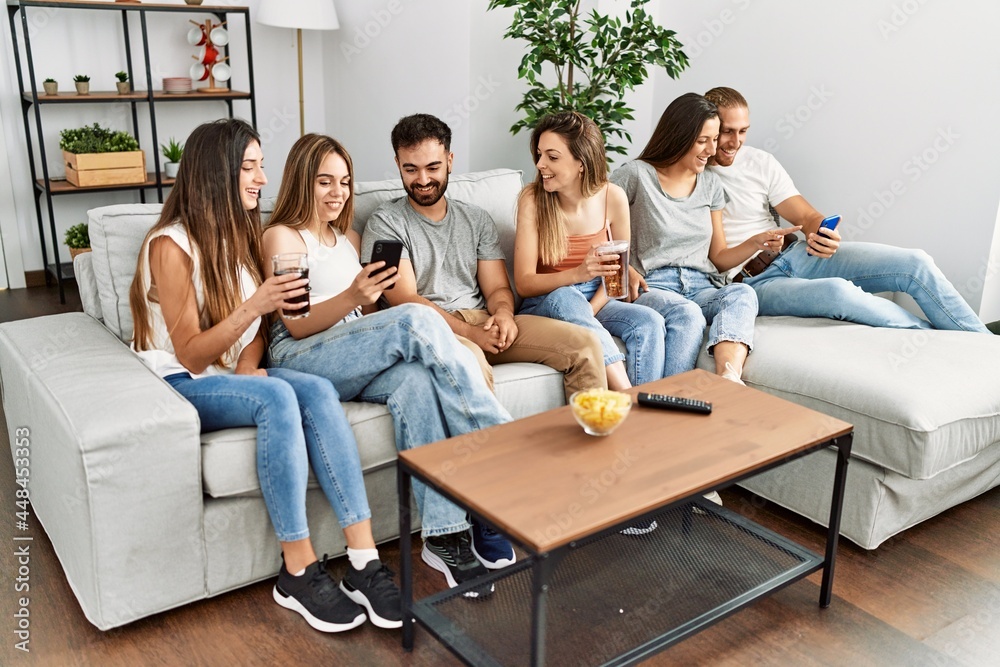 Group of young friends smiling happy and using smartphone sitting on the sofa at home.
