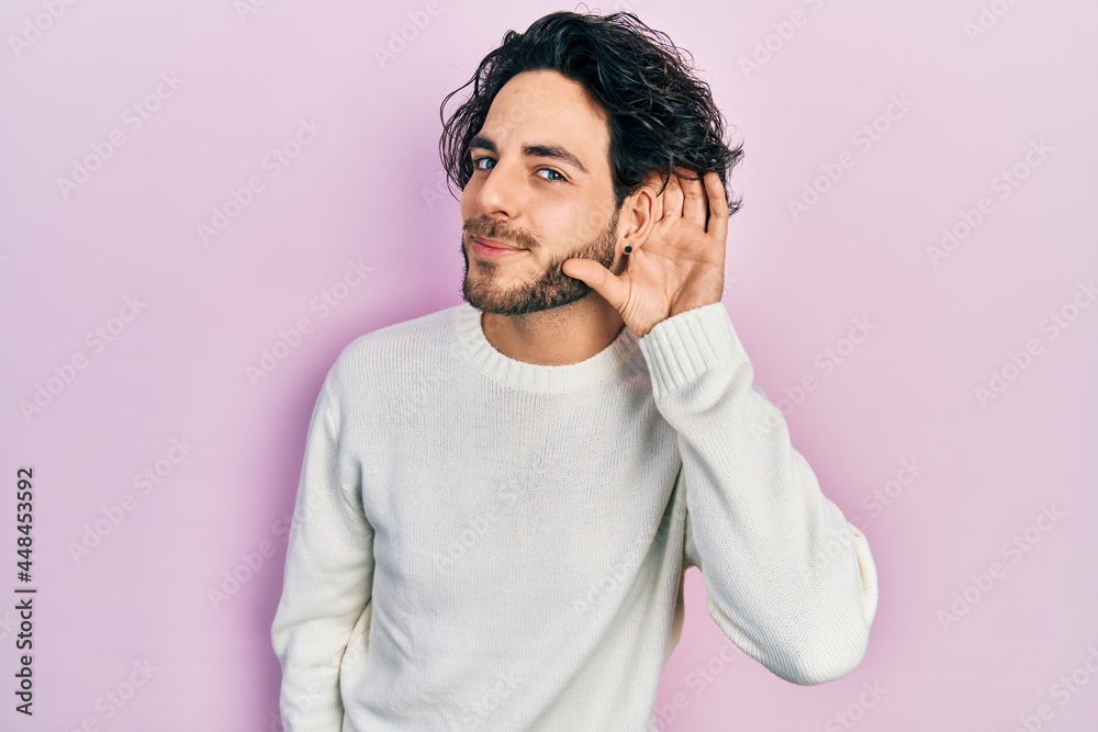 Handsome hispanic man wearing casual white sweater smiling with hand over ear listening an hearing to rumor or gossip. deafness concept. Handsome hispanic man wearing casual white sweater smiling with hand over ear listening an hearing to rumor or gossip. deafness concept.