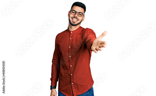 Young hispanic man with beard wearing business shirt and glasses smiling friendly offering handshake as greeting and welcoming. successful business.