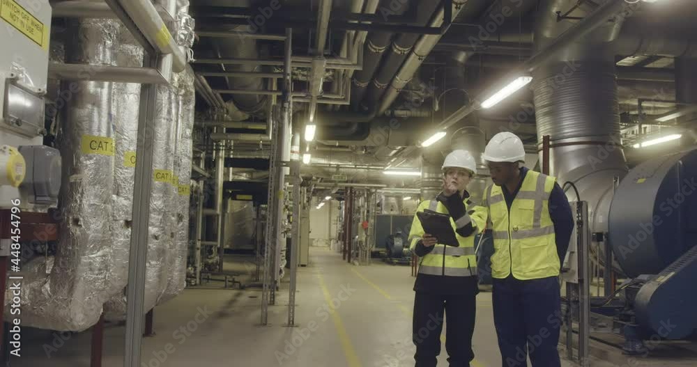 Two engineers working in an industrial plant room Two engineers working in an industrial plant room