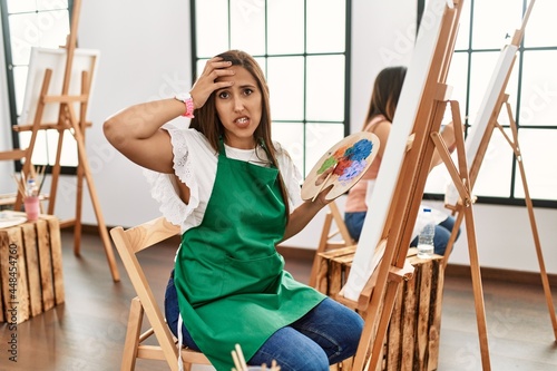 Young hispanic artist women painting on canvas at art studio worried and stressed about a problem with hand on forehead, nervous and anxious for crisis