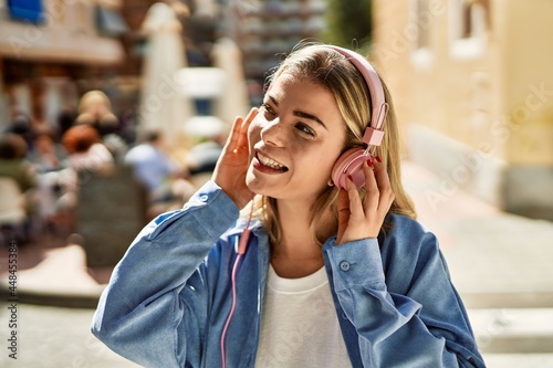 Young blonde girl smiling happy using headphones at the city.