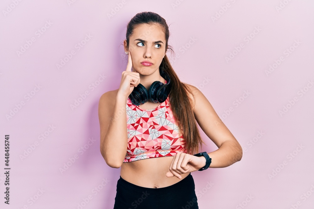 Young brunette teenager wearing gym clothes, using headphones and smart watch serious face thinking about question with hand on chin, thoughtful about confusing idea Young brunette teenager wearing gym clothes, using headphones and smart watch serious face thinking about question with hand on chin, thoughtful about confusing idea