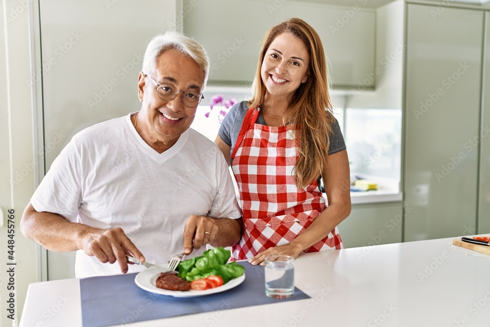 Middle age hispanic couple smiling happy eating beef with salad at the kitchen.