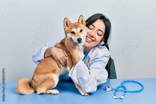 Veterinarian woman wearing uniform at the clinic, hugging dog with love © Krakenimages.com