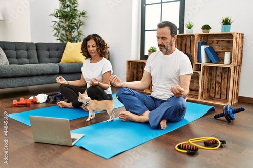 Middle age hispanic couple concentrated doing online yoga class at home.