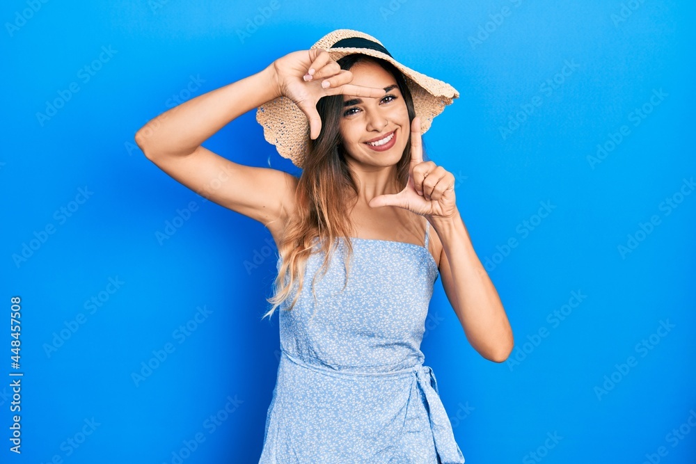 Young hispanic girl wearing summer hat smiling making frame with hands and fingers with happy face. creativity and photography concept. Young hispanic girl wearing summer hat smiling making frame with hands and fingers with happy face. creativity and photography concept.