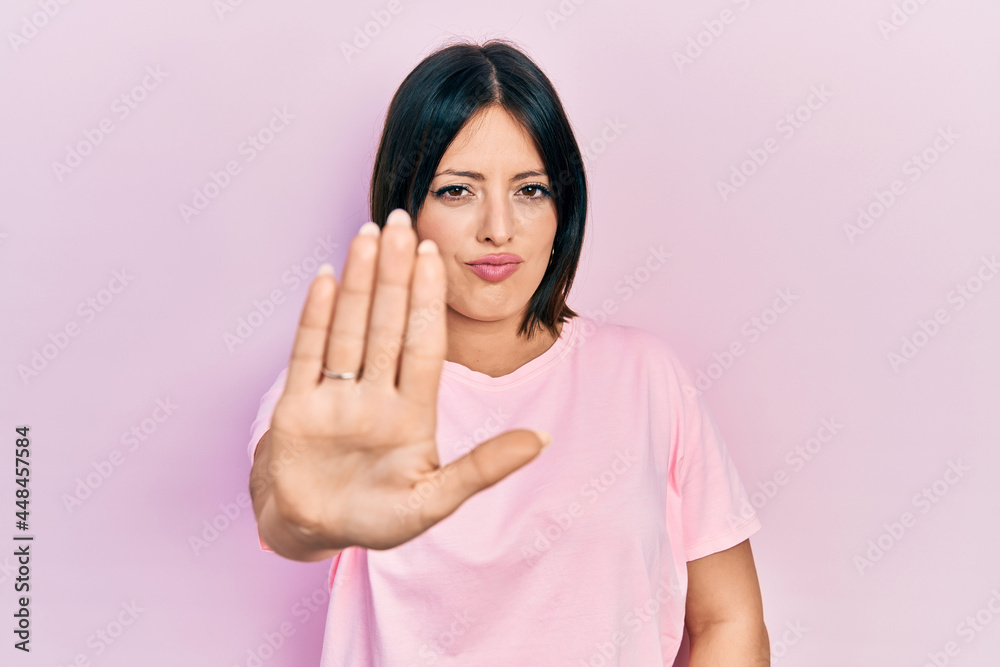 Young hispanic woman wearing casual pink t shirt doing stop sing with palm of the hand. warning expression with negative and serious gesture on the face. Young hispanic woman wearing casual pink t shirt doing stop sing with palm of the hand. warning expression with negative and serious gesture on the face.